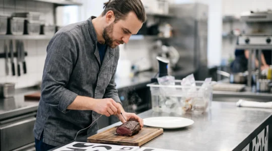 Chef professionnel contrôlant la température à cœur d'une pièce de viande avec une sonde dans une cuisine gastronomique
